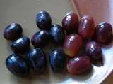 Whole black grapes on the left, whole red grapes on the right, on a brown ceramic plate
