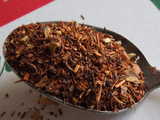 A spoon of spiced rooibos, showing mostly red rooibos leaf and stem with some spices