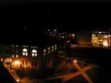 A college campus at night, viewed from high above, showing criss-crossing paths illuminated by orange lights, an old building on the left and modern one on the right