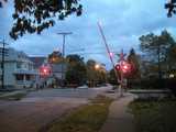 A railroad crossing closing with flashing lights, at dusk, in a residential neighborhood