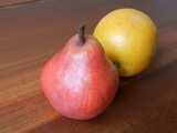 A red pear and a Valencia orange on a wooden surface