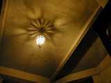 A lamp on an outdoor ceiling, casting a beautiful, complex, symmetrical shadow on the ceiling
