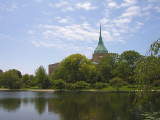 Lake in the foreground, trees along the far shore, and a church with a big steeple rising behind the trees