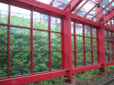 A framework of red metal and glass, with lush green vegetation on a sloping hillside behind