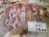 A plastic bin containing whole squid for sale, with a sign reading: SQUID $4.99 LB