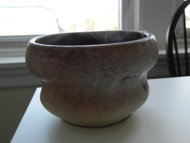 An unusual-shaped mug, handleless, with water vapor rising from above it