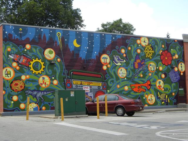 A colorful mural on a brick wall, showing a night sky with a city, and cosmic themes with round dots and an assortment of objects